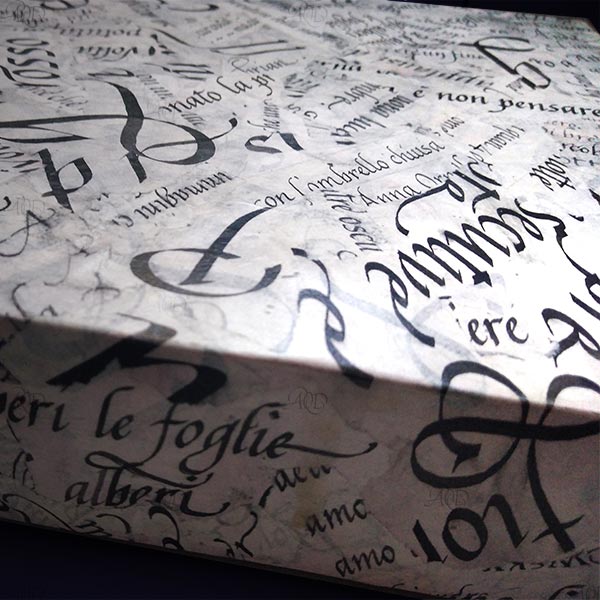 Dettaglio di una scatola su cui sono sovrapposte lettere e parole scritte a mano in scrittura Cancelleresca con inchiostro nero